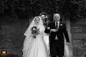 Longstowe Hall, Cambridge, UK, provides the setting as the bride holds her father's arm while they share a final quiet moment walking together toward the ceremony.